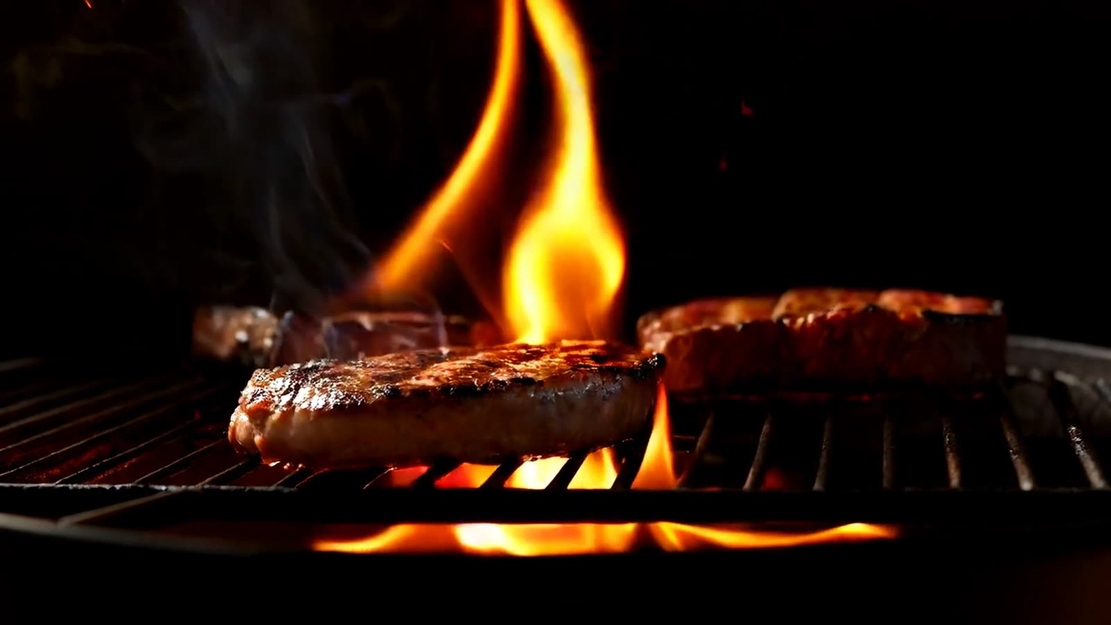 Steaks searing over open flames on a grill